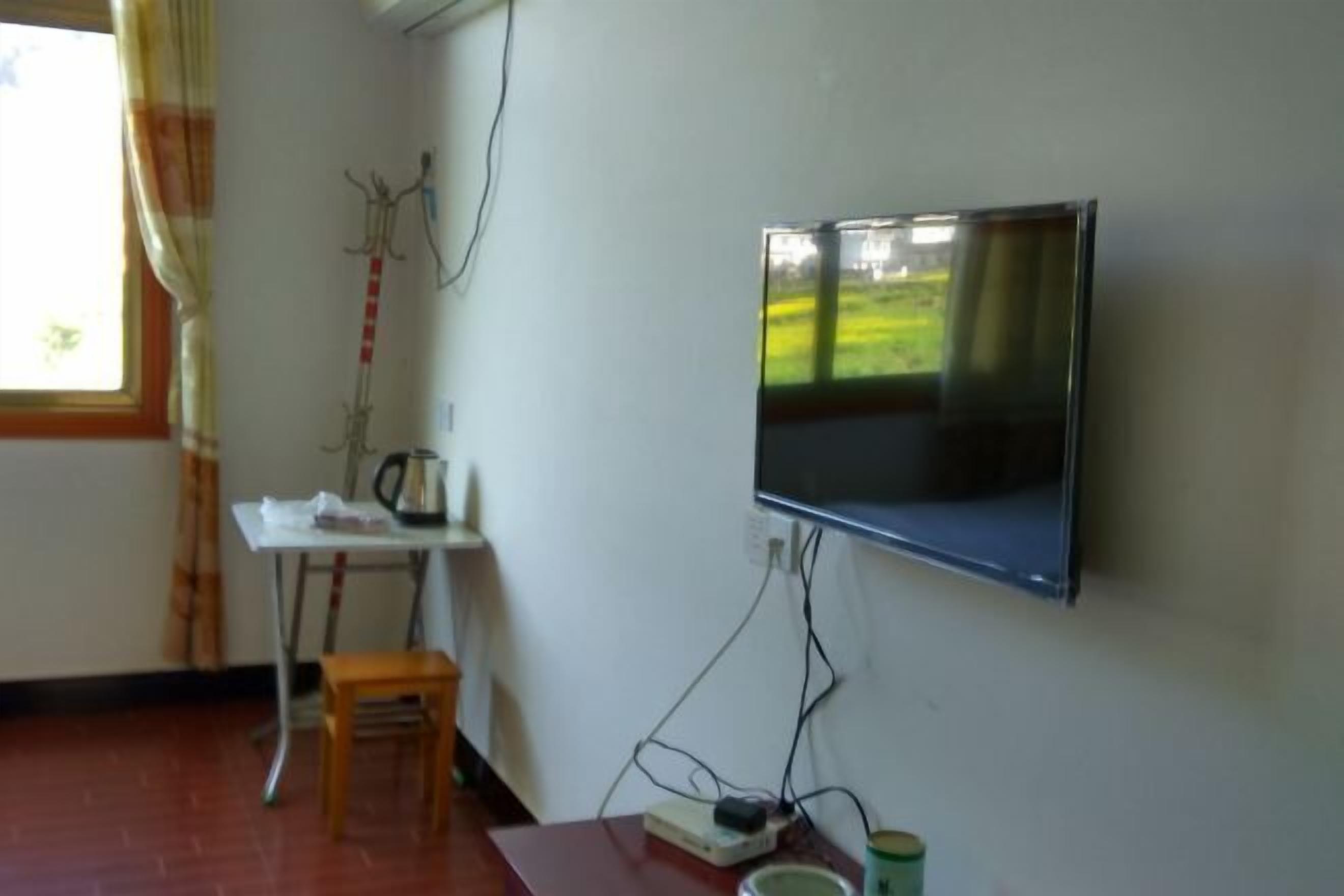 A room with a TV mounted on the wall, a small table with a chair, and a window with curtains.