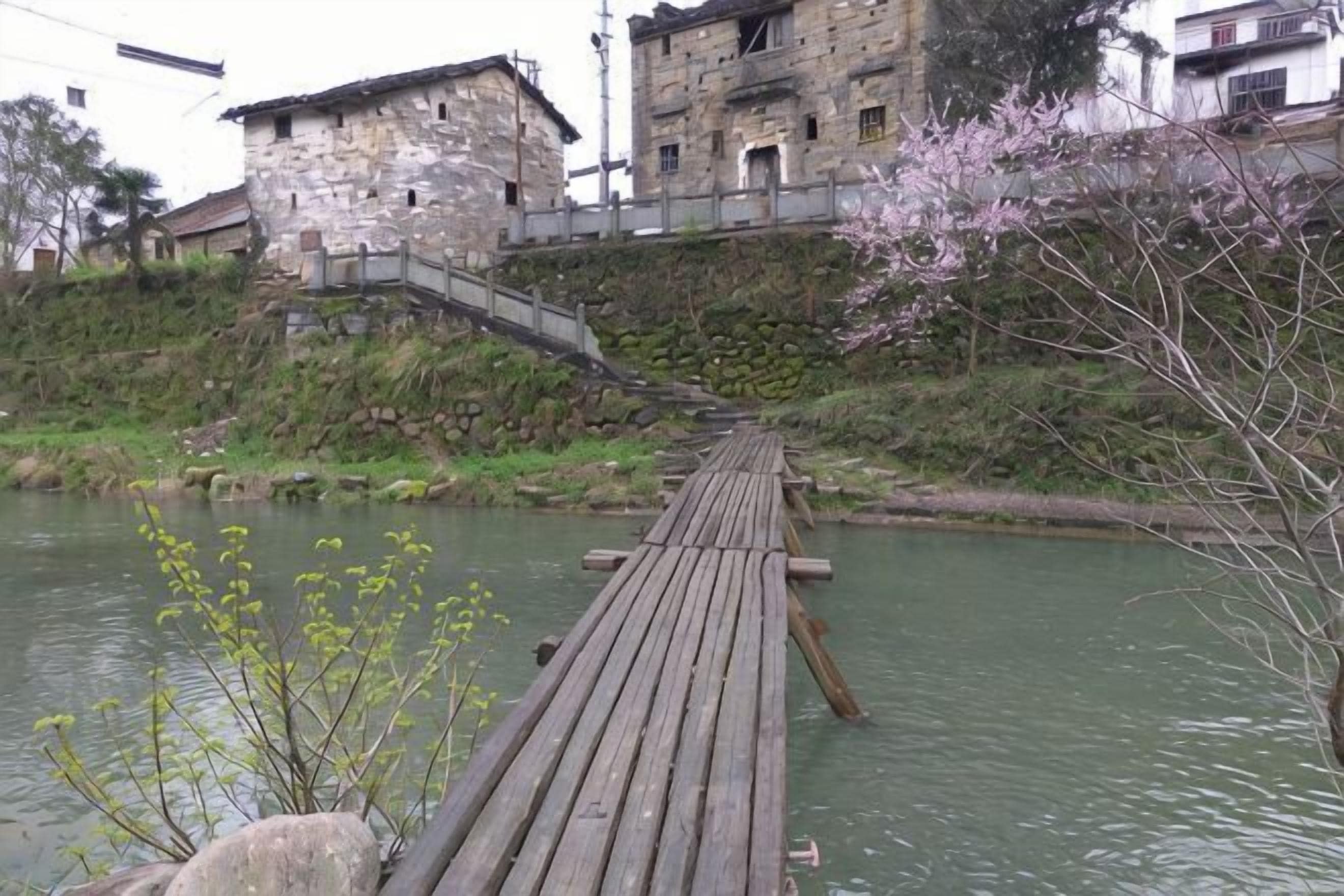 A wooden bridge over a river with stone buildings and a staircase on the left.