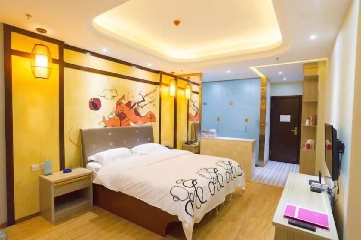 A modern hotel room with a large bed, bedside tables, a desk, and a wall-mounted TV.