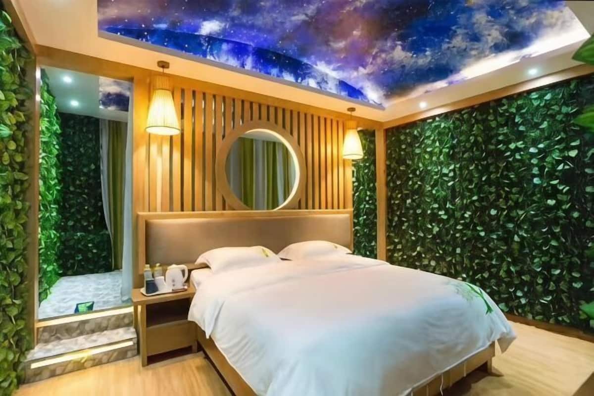 A bedroom with a bed, a nightstand, a mirror, and a wall with a green leafy pattern.
