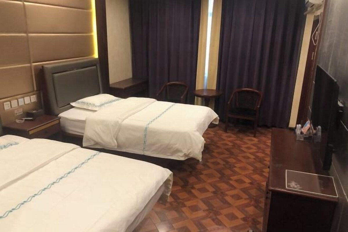 A hotel room with two beds, a TV, a desk, and a window with curtains.