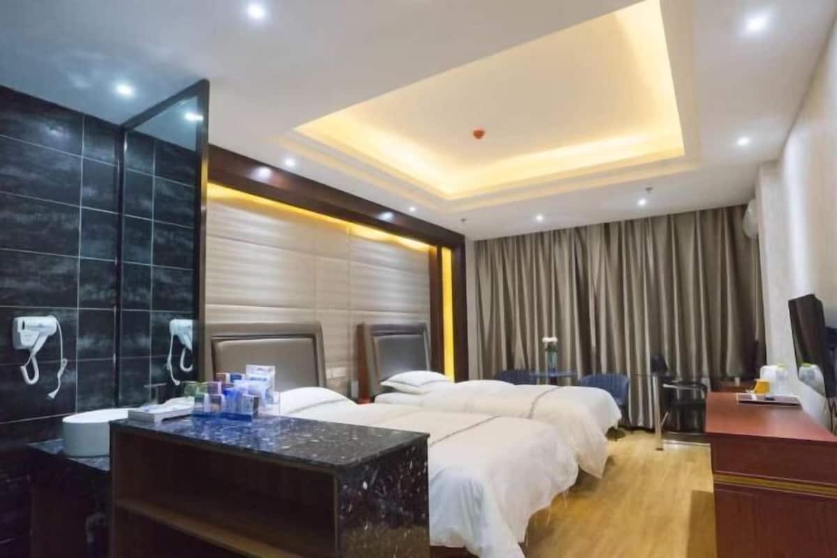 A hotel room with two beds, a desk, a mirror, and a bathroom with a toilet and sink.