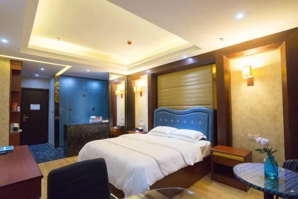 A hotel room with a bed, bedside table, chair, and a small round table with a vase.