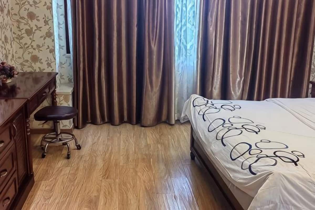 A bedroom with a bed, a wooden dresser, a stool, and a window with curtains.