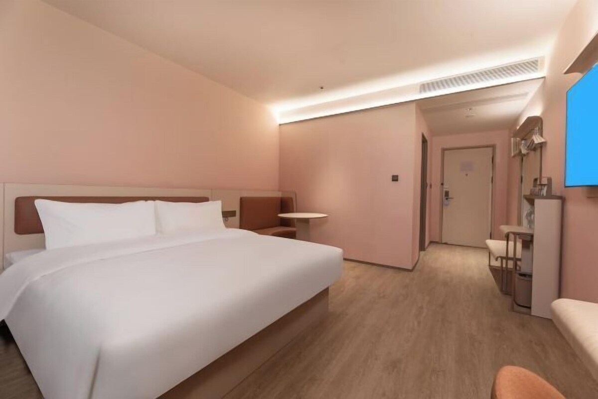 Hotellihuone, jossa on suuri sänky, pieni pöytä, tuoli ja työpöytä, jossa on tietokone.