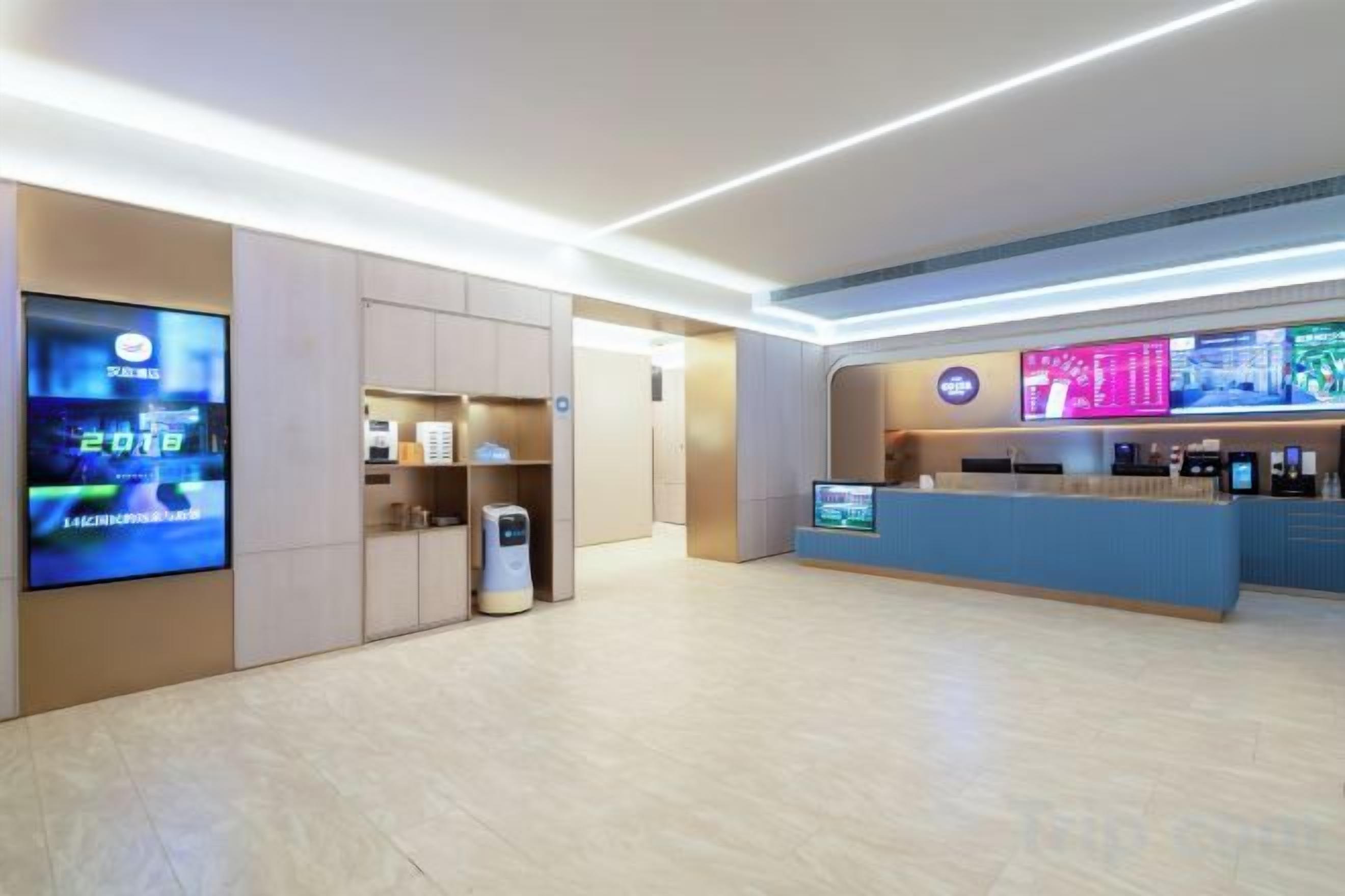 A modern hotel lobby with a reception desk, digital screens, and a self-service kiosk.