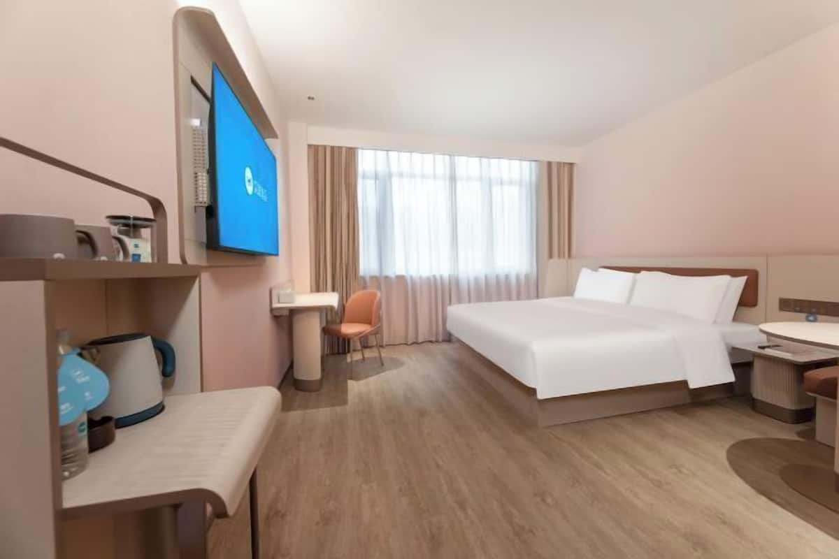 Ein Hotelzimmer mit Bett, Schreibtisch, Stuhl, Fernseher und einem Fenster mit Vorhängen.