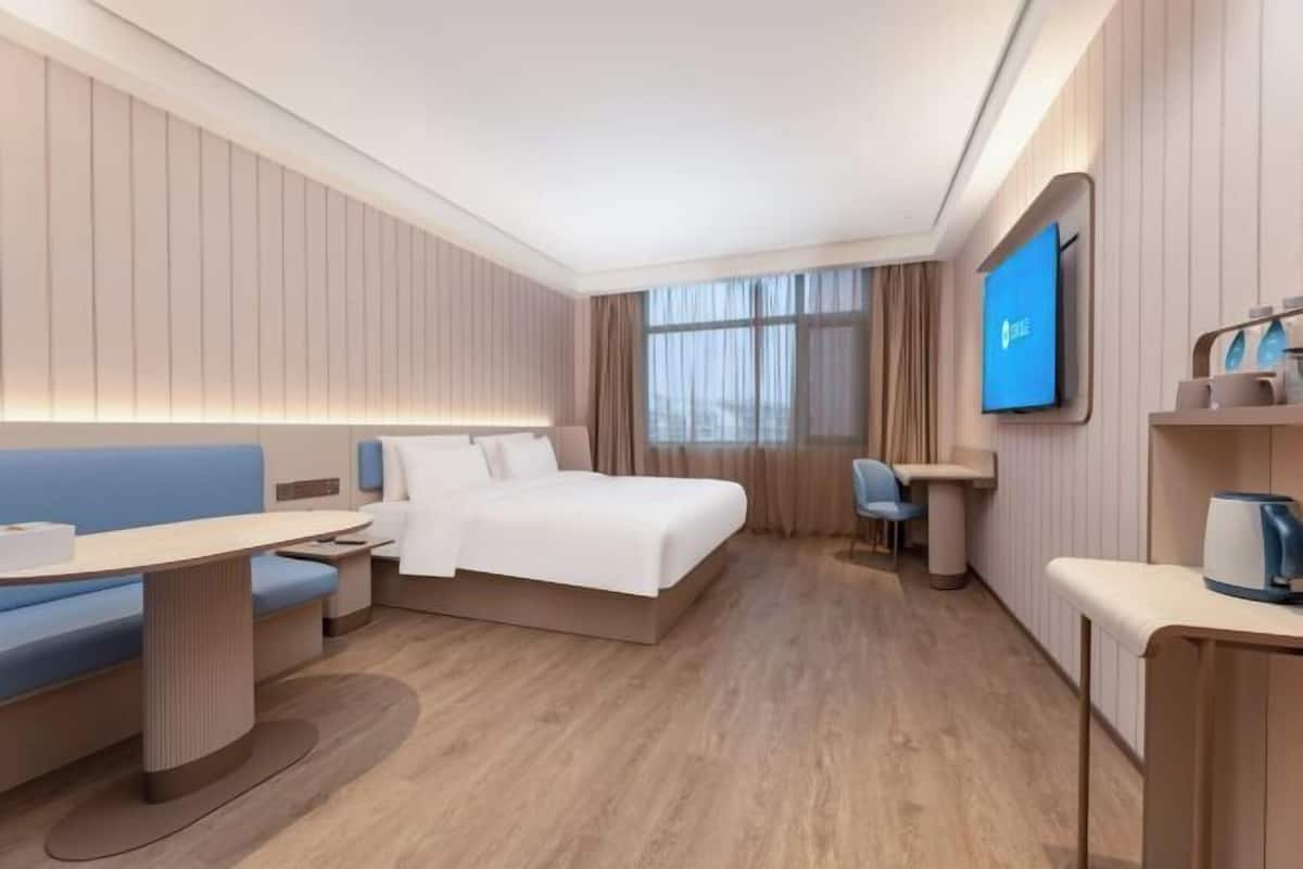 Ein modernes Hotelzimmer mit Bett, Schreibtisch, Stuhl, Fernseher und einem kleinen Tisch mit Wasserkocher.