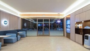 Un hall d’hôtel moderne, doté d’espaces aménagés avec des sièges, d’un comptoir de réception et d’une porte vitrée donnant sur l’extérieur.
