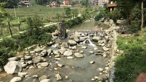Paisaje rural con un arroyo, rocas y una rueda hidráulica.