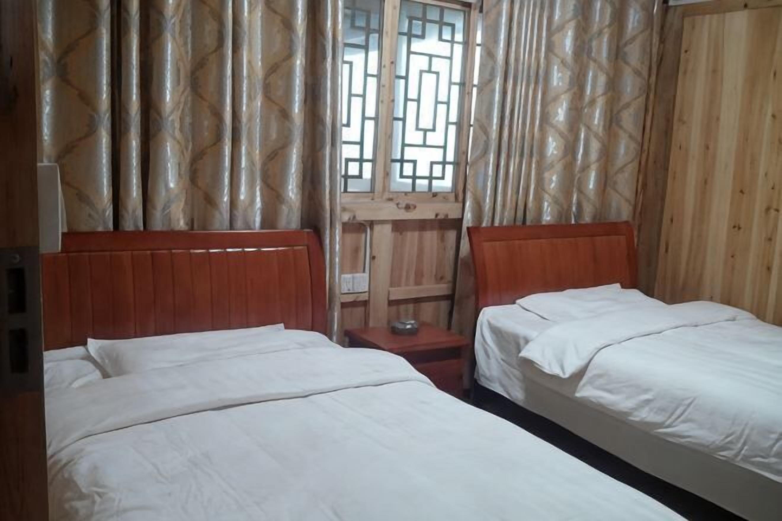 Une chambre avec deux lits, des têtes de lit en bois, une fenêtre ornée d’un motif géométrique et une porte en bois.