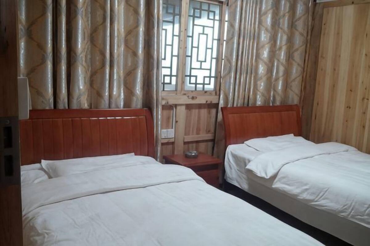 Een kamer met twee bedden, houten hoofdborden, een raam met een geometrisch patroon en een houten deur.