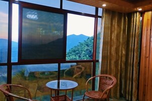 Una habitación con un gran ventanal, una mesa, dos sillas de mimbre y una cortina.