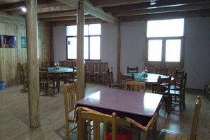A dining area with multiple tables and chairs, wooden beams on the ceiling, and large windows.