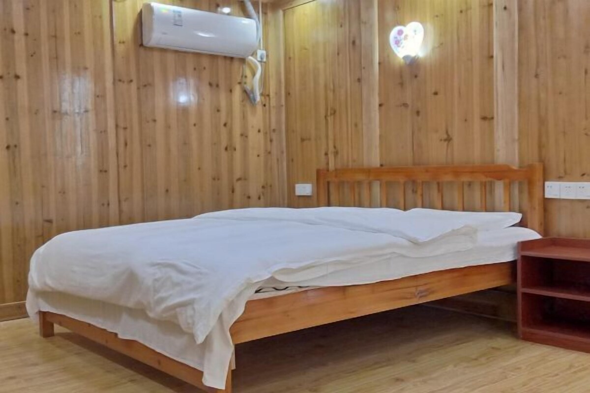 Une pièce aux murs lambrissés, avec un lit simple, une tête de lit en bois et une petite étagère en bois.