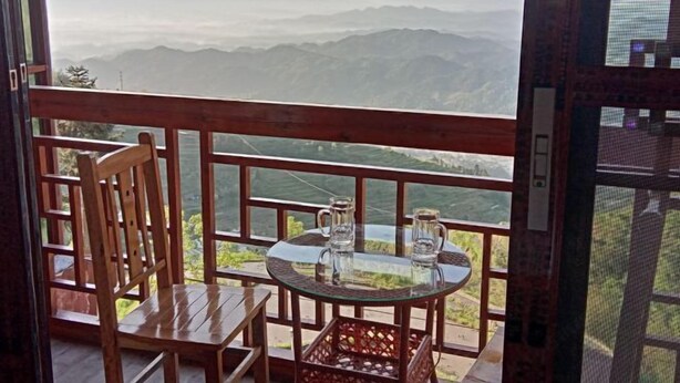 Un balcón con una silla de madera y una mesa de vidrio, con vista a un paisaje montañoso.