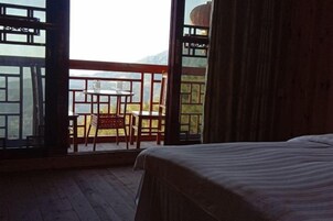 A room with a bed, a table, and chairs near a window overlooking a mountainous landscape.