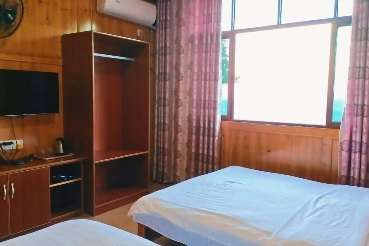 Een kamer met twee bedden, houten wanden, een kledingkast, een televisie en een raam met gordijnen.