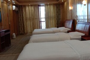 A room with three single beds, wooden walls, a desk, and a window with curtains.