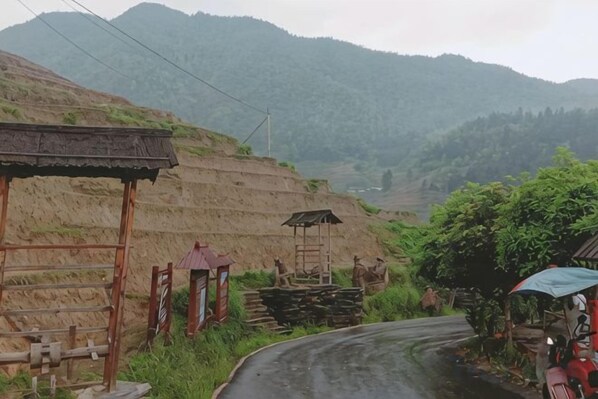 A rural road with terraced fields, a wooden structure, and a small shelter.