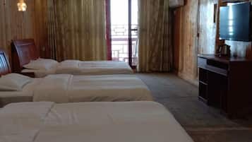 A hotel room with three beds, wooden walls, a television, and a balcony view.