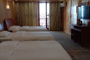 A hotel room with three beds, wooden walls, a television, and a balcony view.