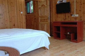 Une pièce en bois avec un lit, un téléviseur fixé au mur et un petit meuble rouge.