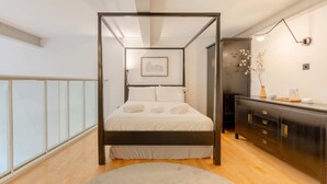 Une chambre moderne avec un lit à baldaquin, un plancher en bois, une commode sombre et un tableau encadré accroché au mur.