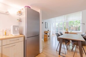 A modern kitchen with a stainless steel refrigerator, wooden cabinets, and a dining area with a table and chairs.