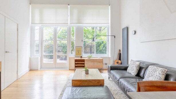 Un salon spacieux doté d’une grande fenêtre, d’un canapé en cuir foncé, d’une table basse en bois et d’un design minimaliste.