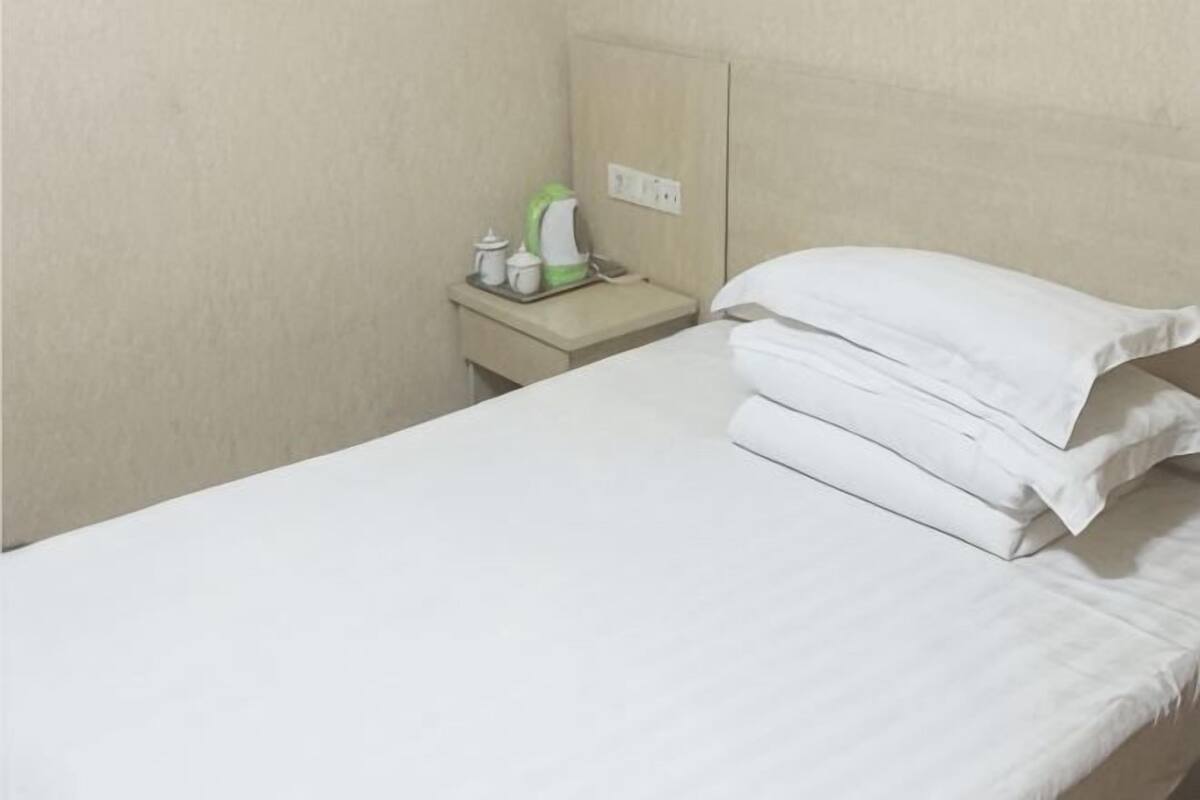 A hotel room with a bed, a nightstand, and a kettle.