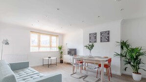 A modern living room with a sofa, dining table, chairs, and potted plants. - Spacious 3BD Flat, Close to Tube - Fulham! (London)
