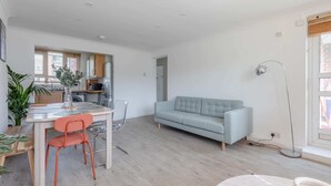 A modern living room with a sofa, dining table, chairs, and a floor lamp. - Spacious 3BD Flat, Close to Tube - Fulham! (London)