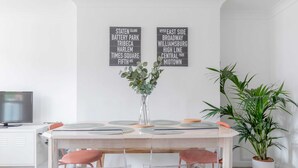 A dining area with a wooden table, clear chairs, and a vase with green foliage. Two wall art pieces with text are visible. - Spacious 3BD Flat, Close to Tube - Fulham! (London)