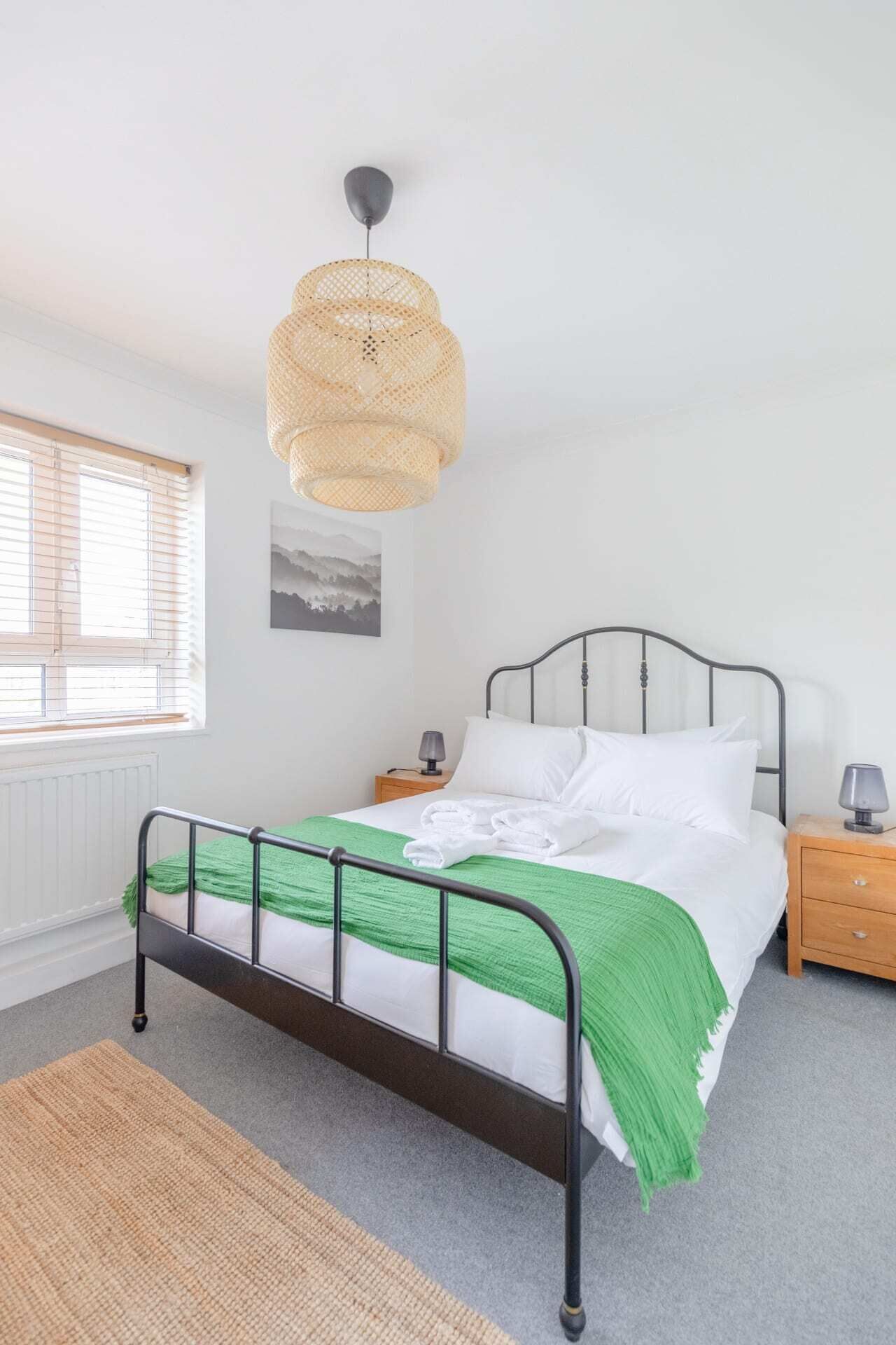 A neatly arranged bedroom with a bed, bedside tables, a hanging light fixture, and a window with blinds.