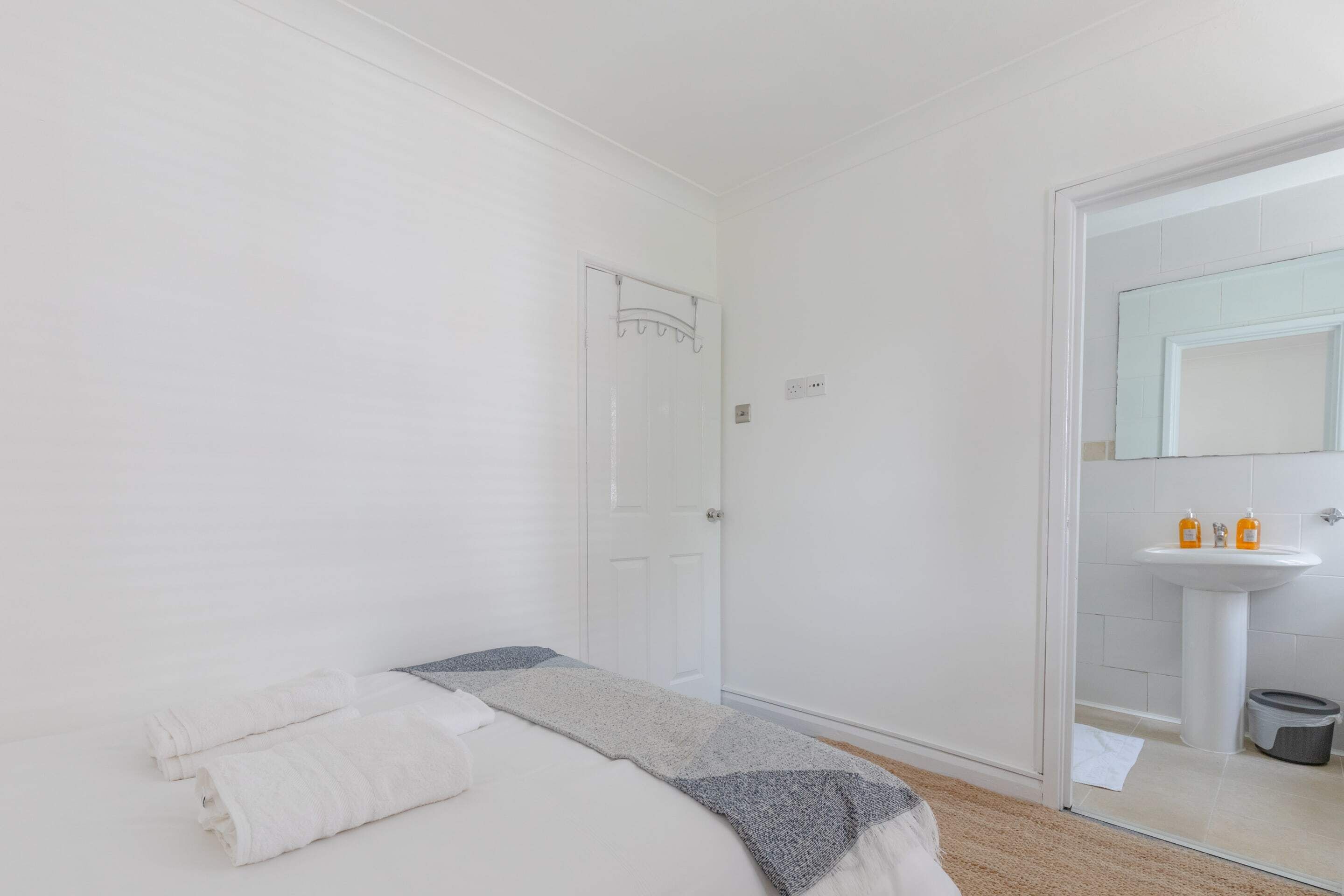 Una habitación de hotel con una cama, una mesita de noche, un espejo y un baño visible a través de una puerta abierta.