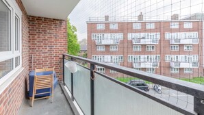 A balcony with a view of a brick building, a chair, and a hanging light fixture. - Spacious 3BD Flat, Close to Tube - Fulham! (London)