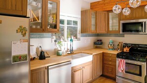 Eine moderne Küche mit Holzschränken, einem Edelstahlkühlschrank, einer Spüle, einem Herd und einem Fenster mit Blick ins Freie.