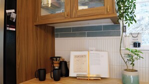 Eine Küche mit Holzausstattung, einer Kaffeemaschine, einer schwarzen Tasse, einem Blumentopf und einer Speisekarte auf der Arbeitsfläche.
