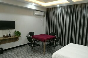 Een hotelkamer met een bed, een aan de muur bevestigde televisie, een tafel met stoelen en een gordijn.