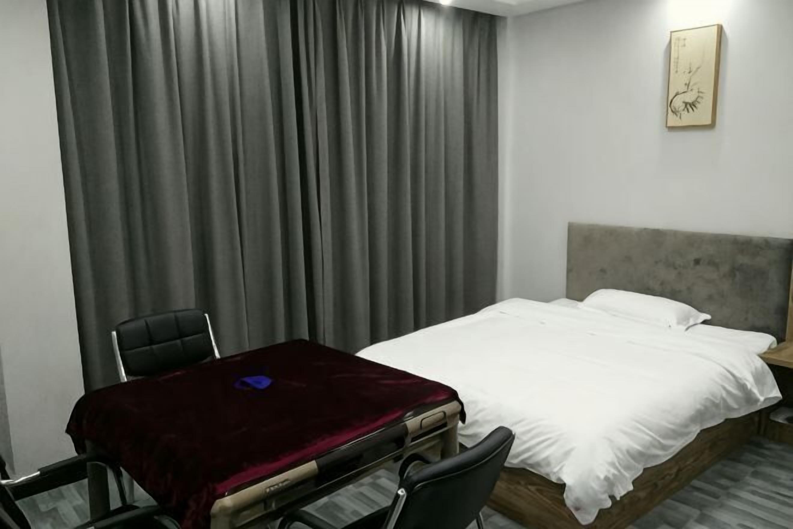 A hotel room with a bed, a desk with a chair, and a large window with curtains.