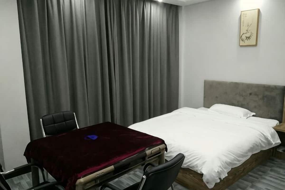 A hotel room with a bed, a desk with a chair, and a large window with curtains.