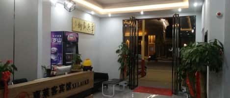 Un espace d’accueil d’hôtel comprenant un comptoir de réception, une affiche et une porte vitrée donnant accès à l’intérieur.