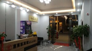 Un espace d’accueil d’hôtel comprenant un comptoir de réception en bois, un coin salon et une porte vitrée donnant sur l’intérieur.