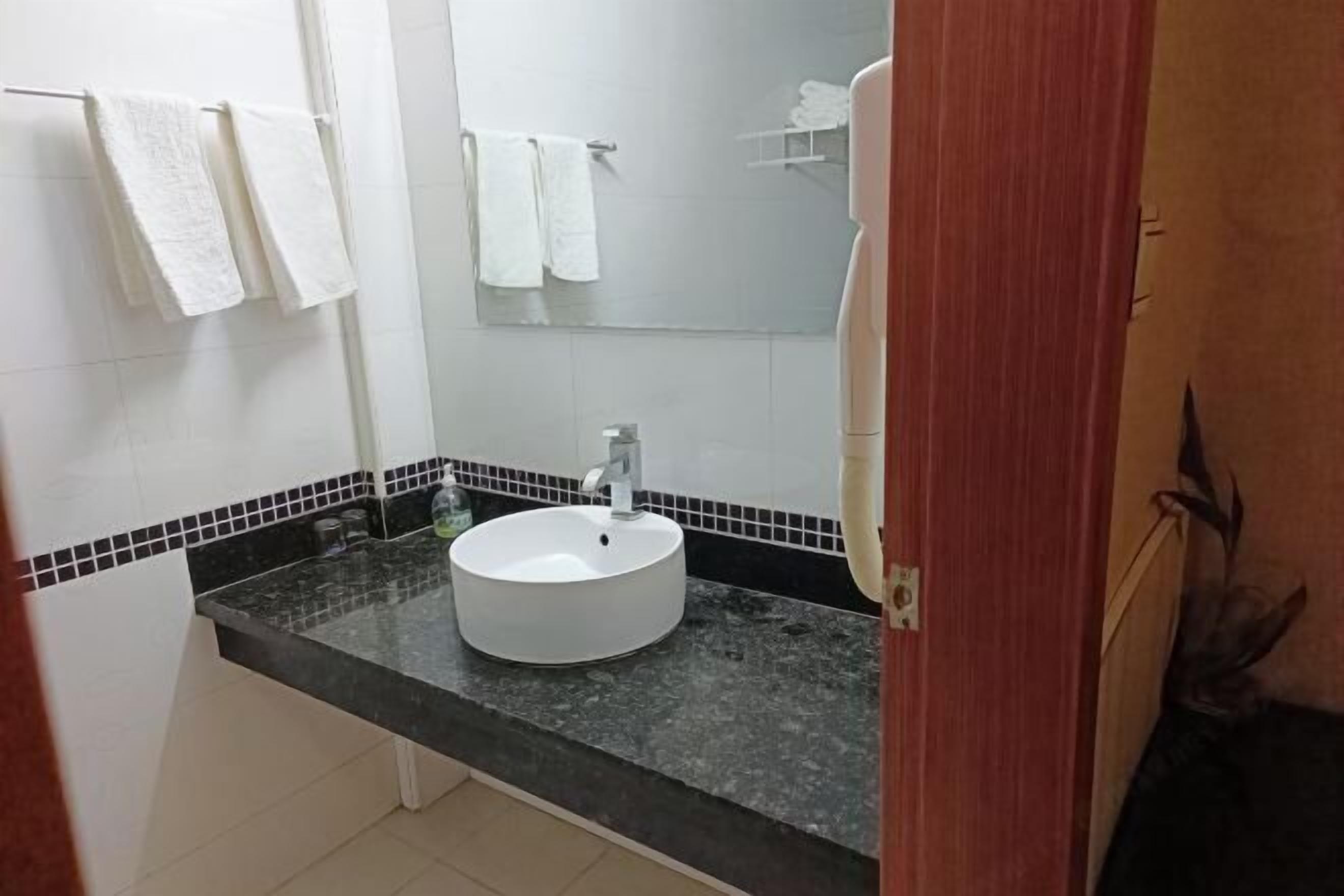 Un baño con lavamanos blanco, encimera negra y paredes cubiertas de azulejos blancos.