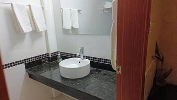 Un baño con lavamanos blanco, encimera negra y paredes cubiertas de azulejos blancos.