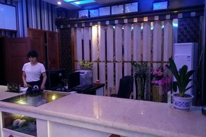 A reception desk with a computer, a potted plant, and a refrigerator. - Daishan Xiushan Hotel (Daishan)