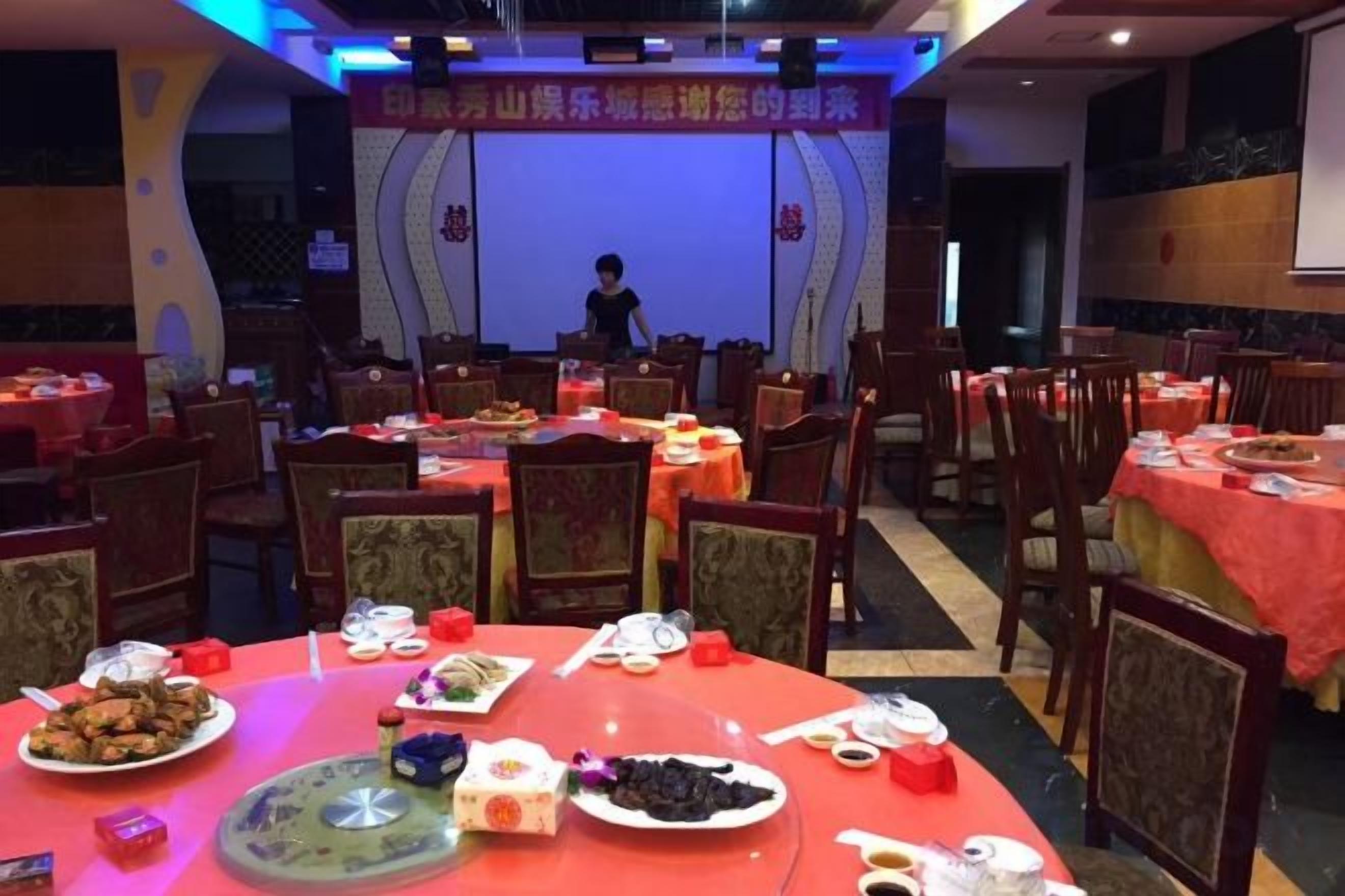 A banquet hall with round tables set for a meal, a stage at the front, and chairs arranged around the tables.