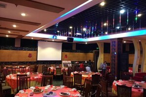 Un comedor con mesas dispuestas para comidas, una pantalla de proyector y un escenario para presentaciones.