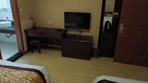 Et hotelværelse med en seng, et skrivebord med et fladskærms-TV, en lille stol og et garderobeskab.